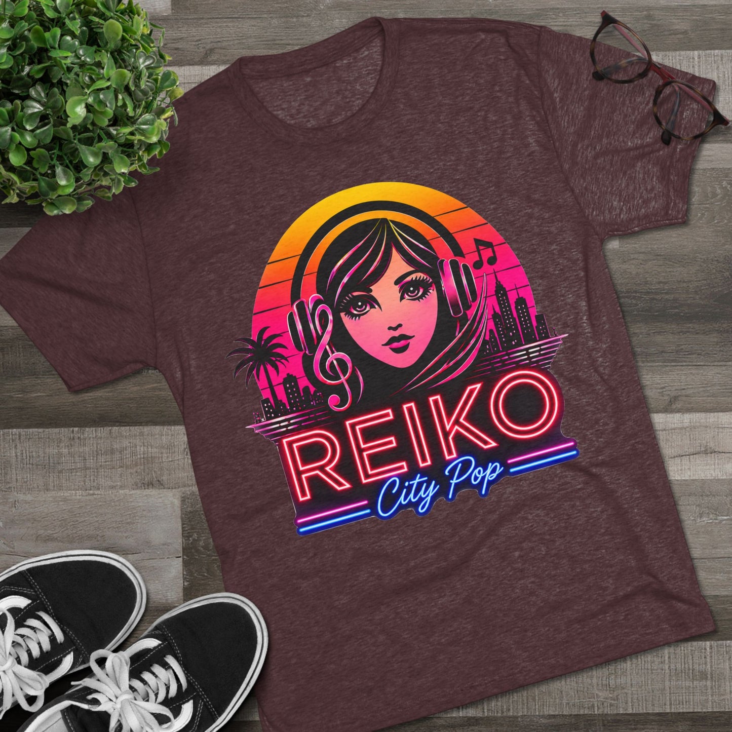 Front view of the Reiko Takahashi City Pop Sunset Logo Tee in Cardinal Black, printed on a premium Next Level tri-blend T-shirt and displayed in a styled flat lay with sneakers, eyeglasses, and a green plant. Features retro neon artwork inspired by the song "Sunset Road."