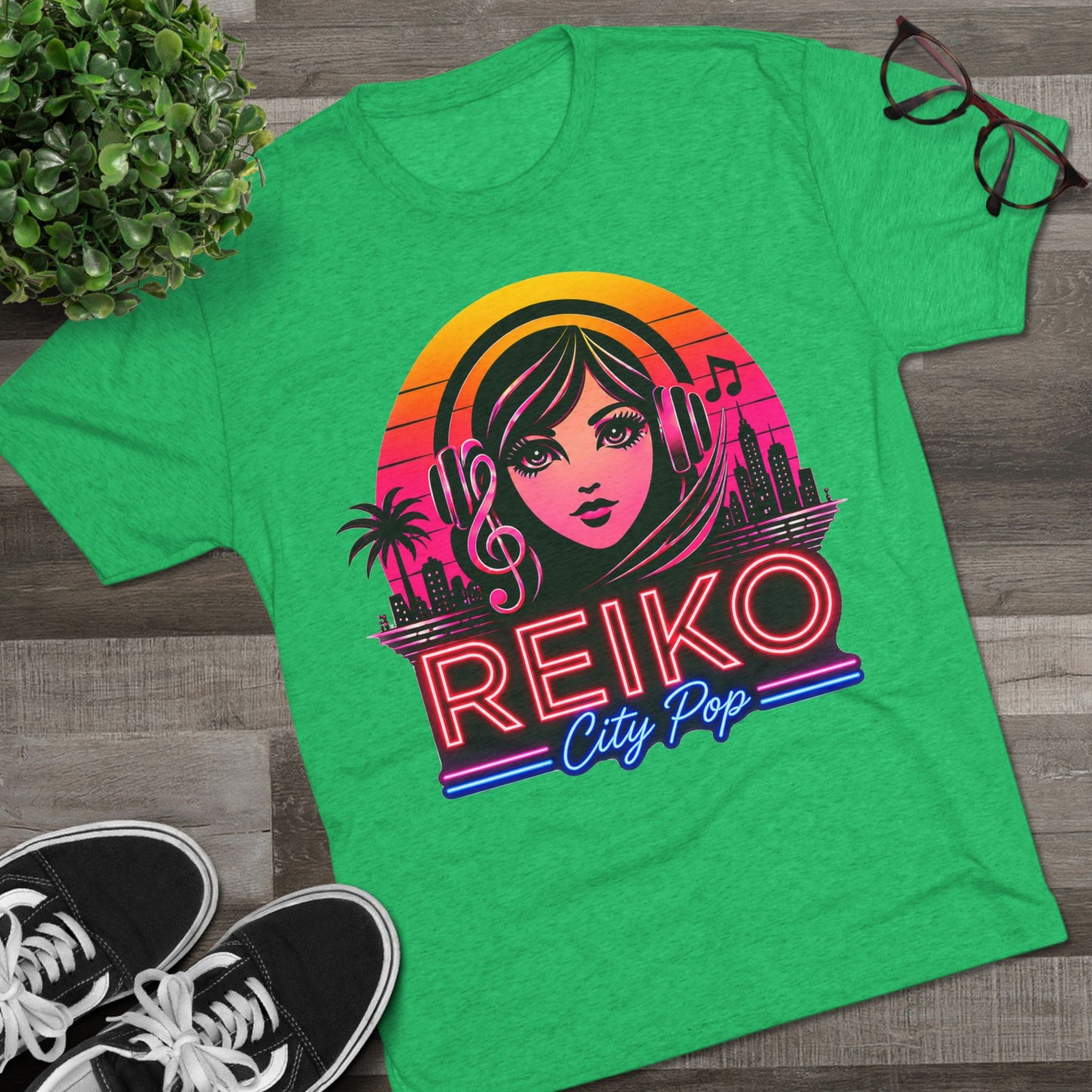 Front view of the Reiko Takahashi City Pop Sunset Logo Tee in Envy Green, printed on a premium Next Level tri-blend T-shirt and displayed in a styled flat lay with sneakers, eyeglasses, and a green plant. Features retro neon artwork inspired by the song "Sunset Road."