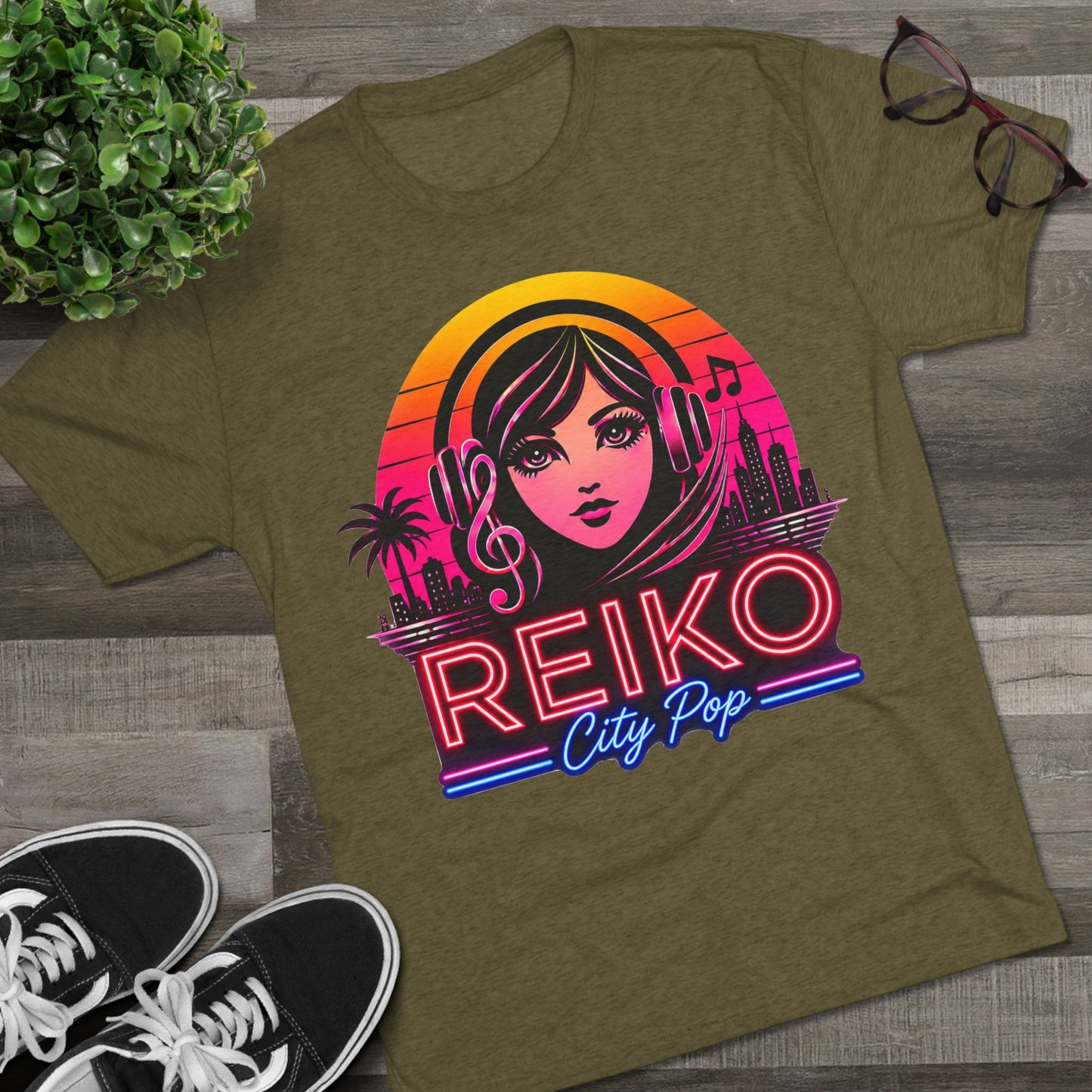 Front view of the Reiko Takahashi City Pop Sunset Logo Tee in Military Green, printed on a premium Next Level tri-blend T-shirt and displayed in a styled flat lay with sneakers, eyeglasses, and a green plant. Features retro neon artwork inspired by the song "Sunset Road."