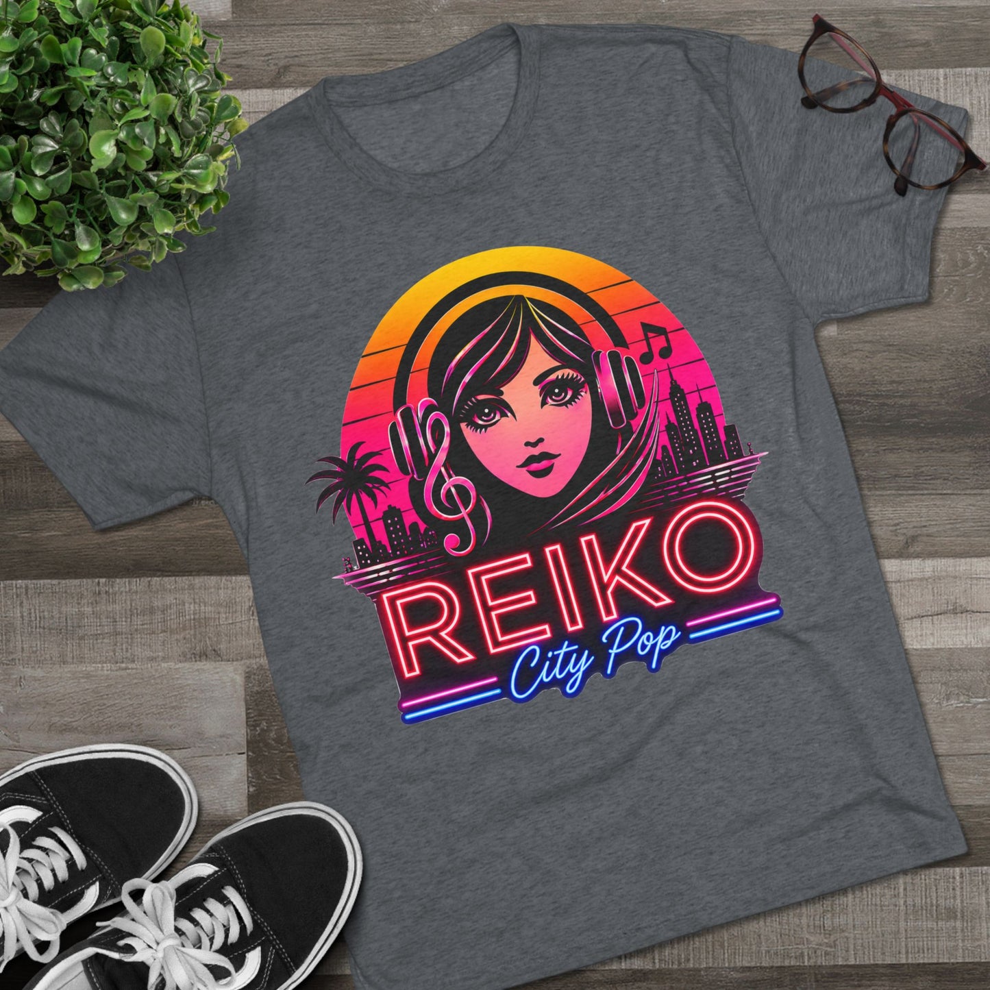Front view of the Reiko Takahashi City Pop Sunset Logo Tee on Premium Heather, printed on a Next Level tri-blend T-shirt and displayed in a styled flat lay with sneakers, eyeglasses, and a green plant. Features retro neon artwork inspired by the song "Sunset Road."