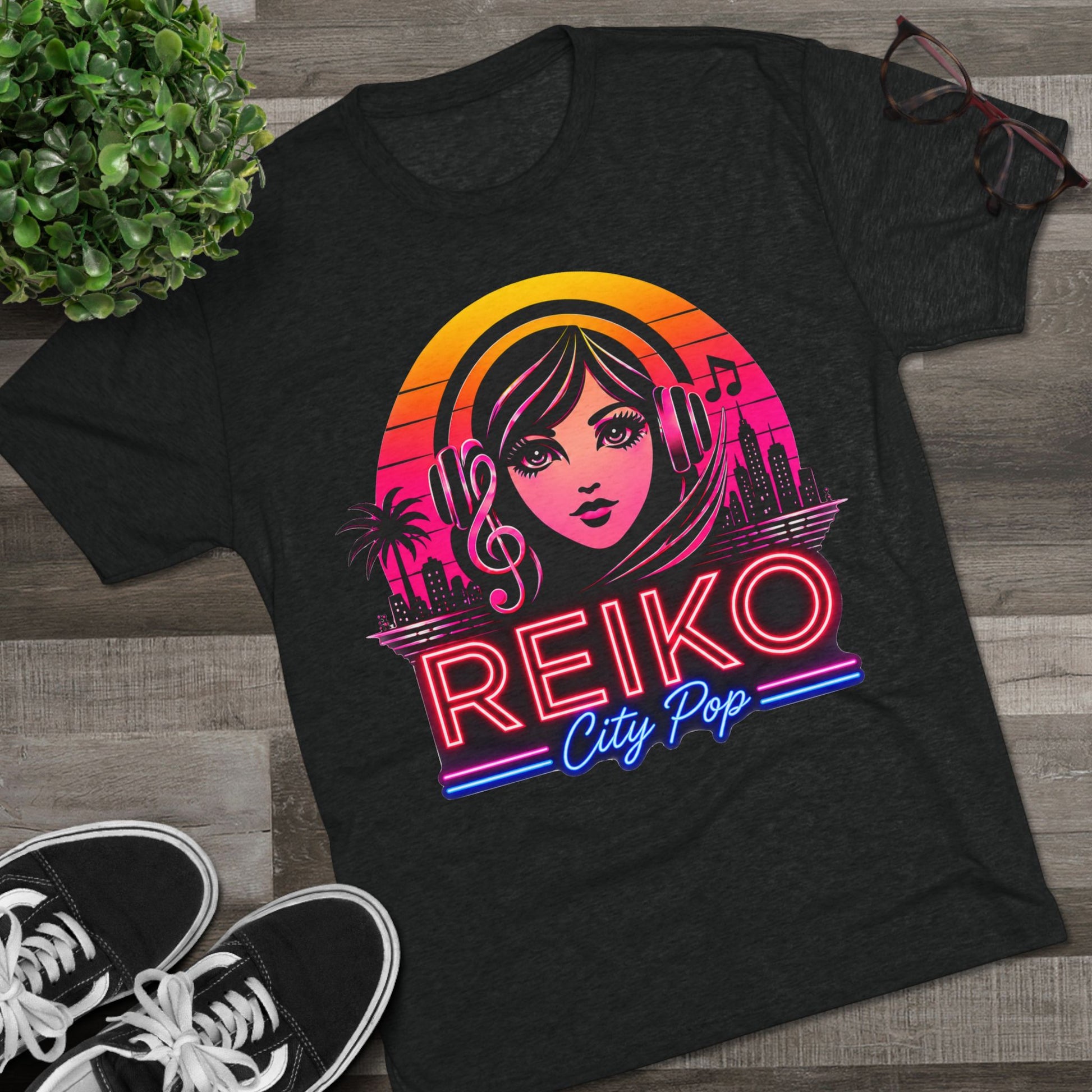 Front view of the Reiko Takahashi City Pop Sunset Logo Tee in Vintage Black, printed on a premium Next Level tri-blend T-shirt and displayed in a styled flat lay with sneakers, eyeglasses, and a green plant. Features retro neon artwork inspired by the song "Sunset Road."