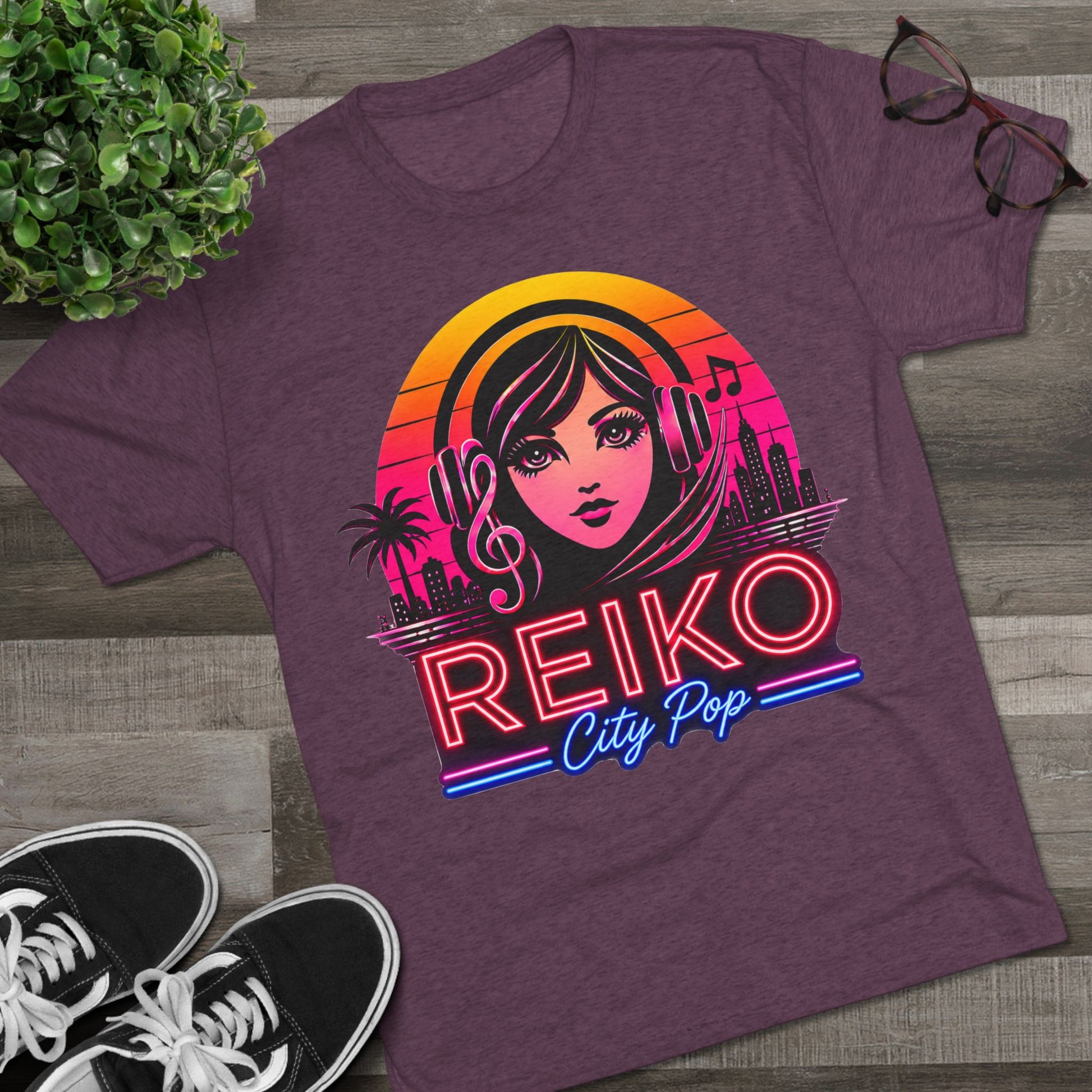 Front view of the Reiko Takahashi City Pop Sunset Logo Tee in Vintage Purple, printed on a premium Next Level tri-blend T-shirt and displayed in a styled flat lay with sneakers, eyeglasses, and a green plant. Features retro neon artwork inspired by the song "Sunset Road."